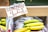 A display shelf holds a bunch of bananas, with a price tag indicating £1.79 per kilogram from the Dominican Republic. The bananas are in plastic bags, with some still green and others ripe yellow.