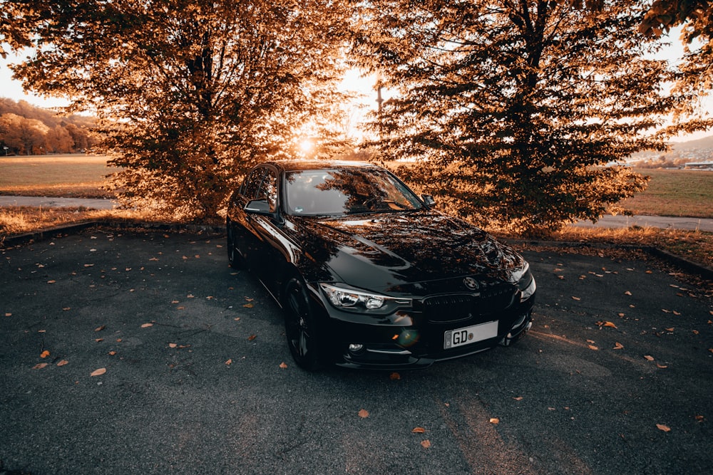 a black car parked in a parking lot next to trees