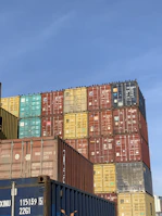 Stacked shipping containers in vibrant colors at a large logistics yard.