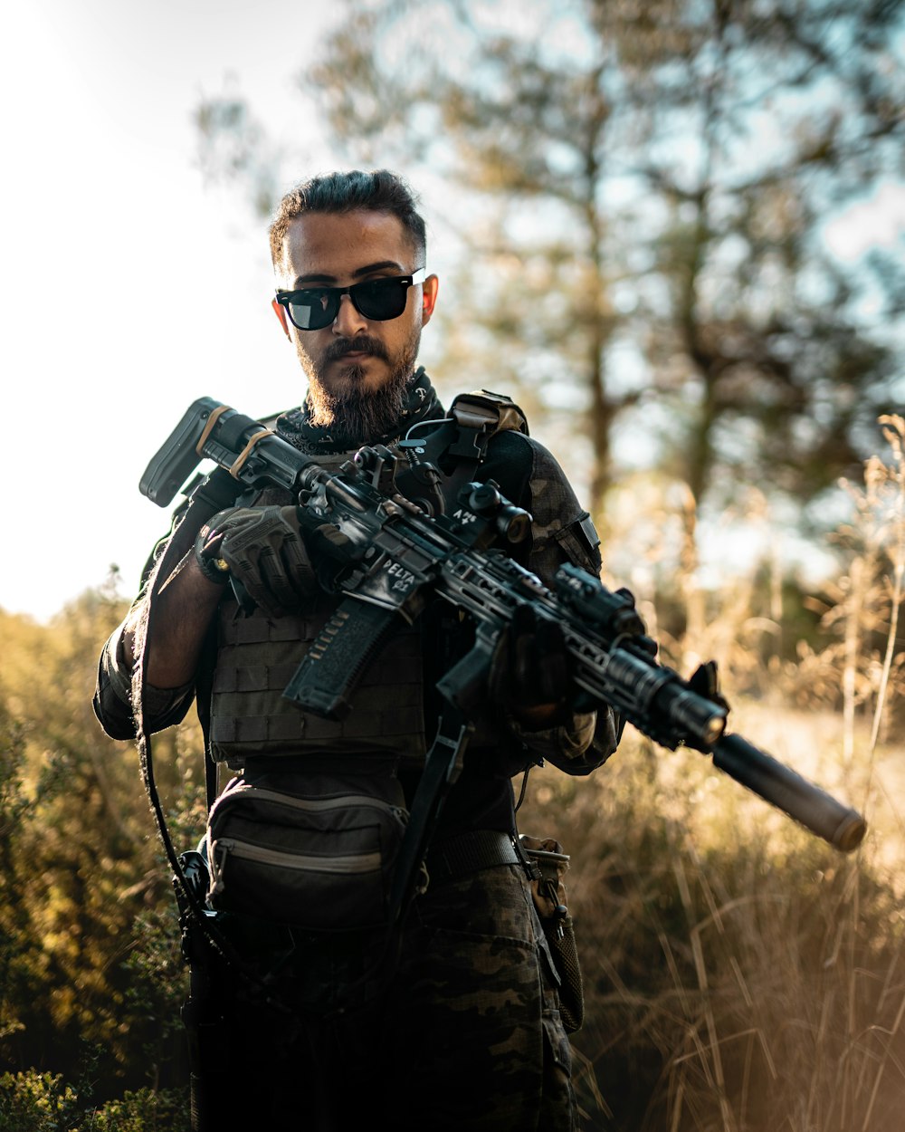 Un homme avec une barbe et des lunettes de soleil tenant une arme à feu