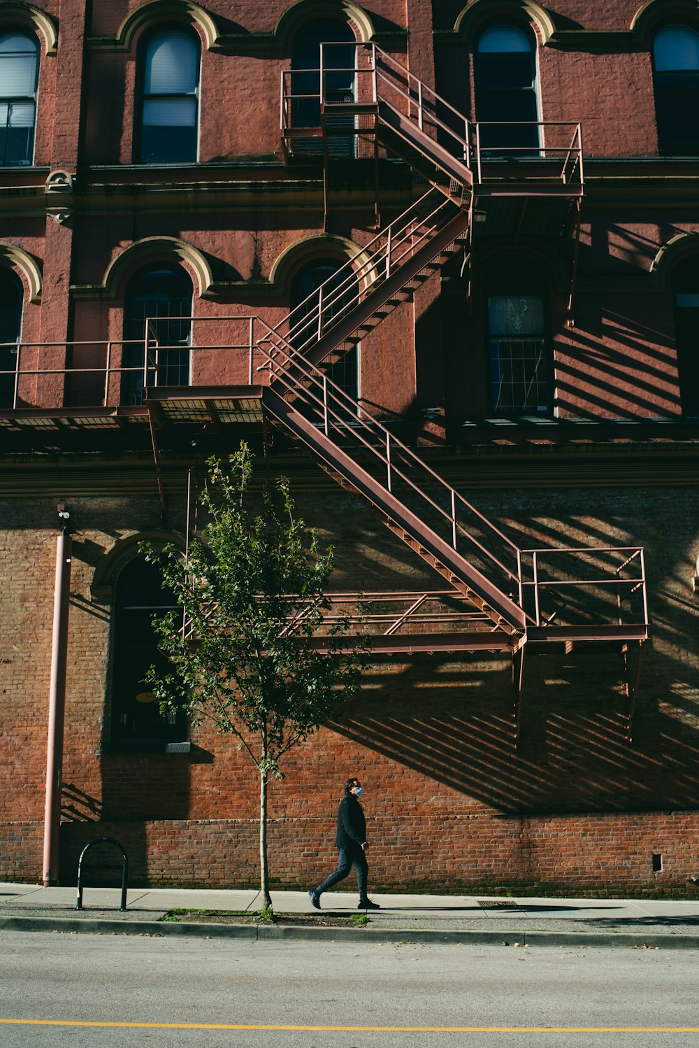 a man walking down a street past a tall brick building