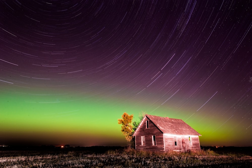 a house in the middle of a field under a star filled sky