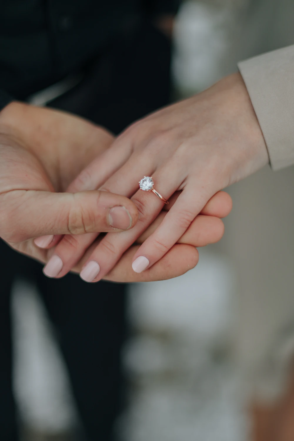 Adult couple holding hands in low light showing an engagement ring and wedding band