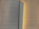 An open book lies flat, displaying pages 10 and 11. The text is well-lit, with a shadow and sunlight creating a contrast on the right side. The narrative appears to be about a cafe closing down, daily routines, and personal reflections.