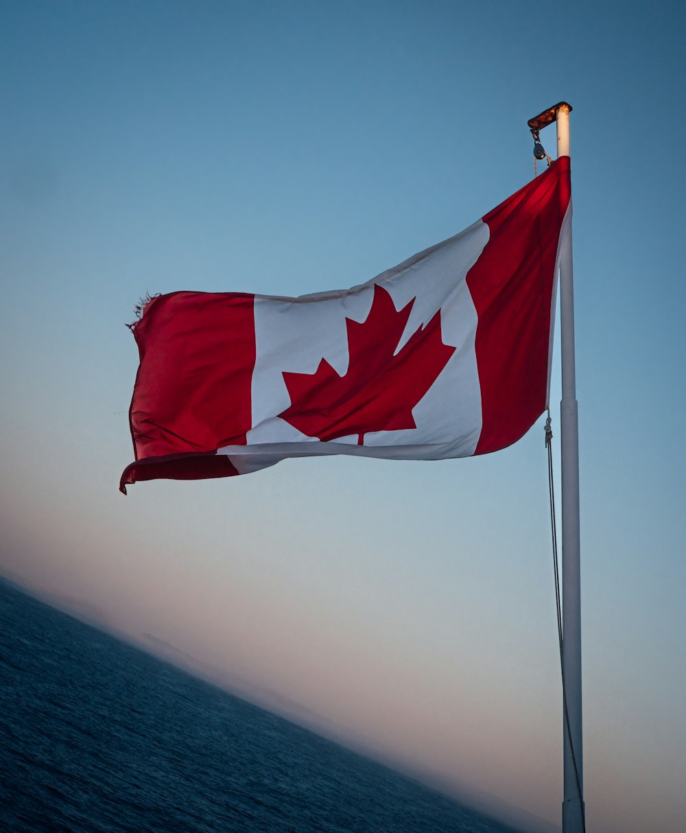 a canadian flag flying in the wind over a body of water