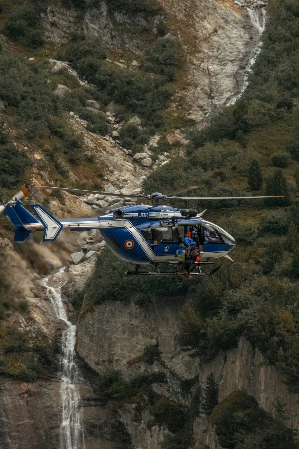 a blue and white helicopter flying over a waterfall