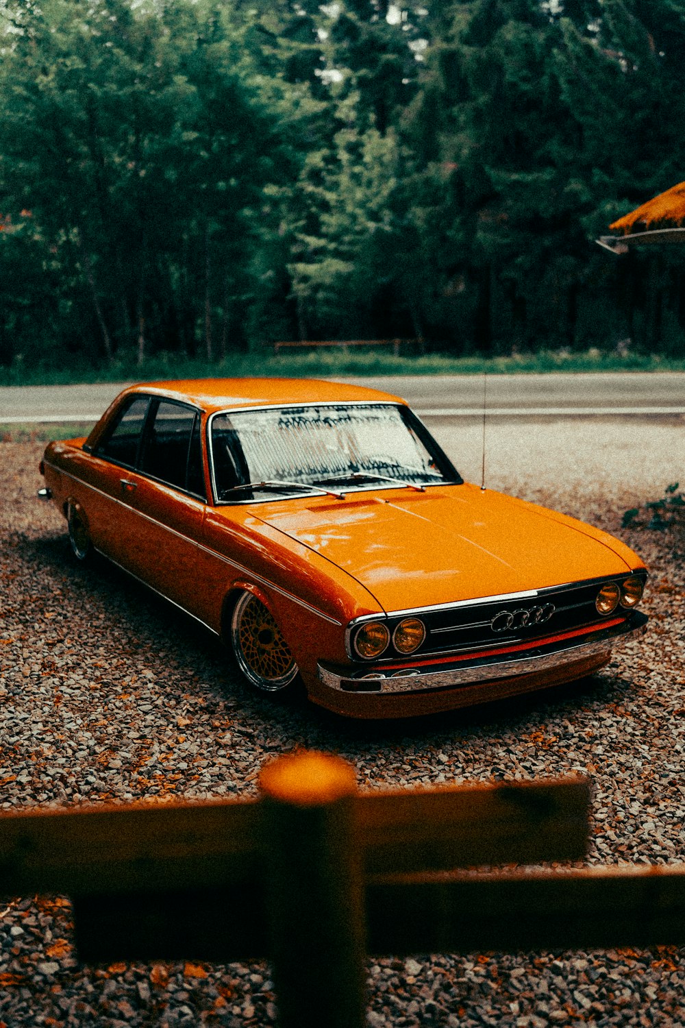 Un coche naranja aparcado en un camino de grava