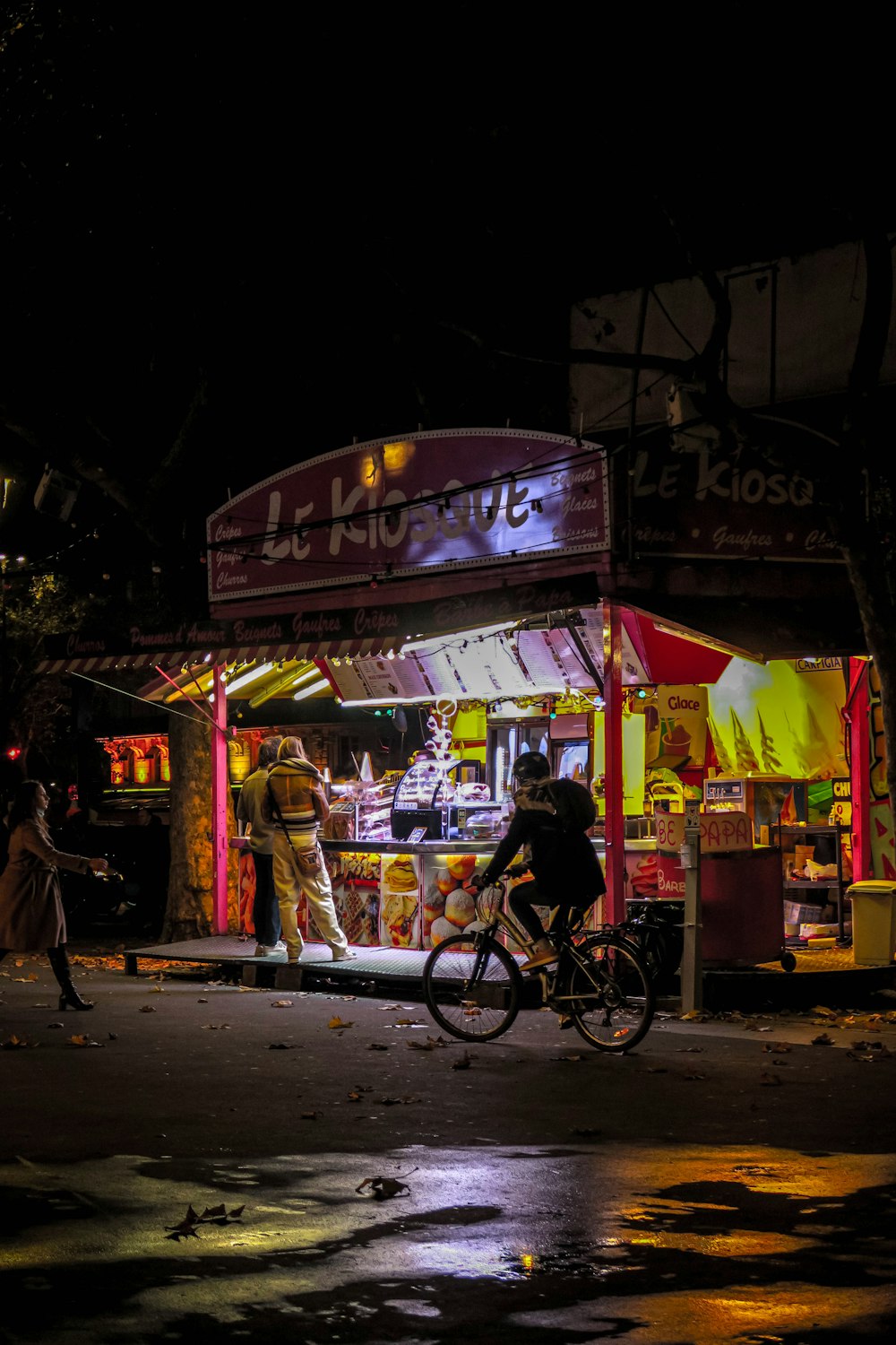 a man riding a bike past a kiosk at night