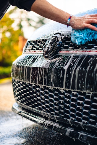 a person washing a black car with a blue rag
