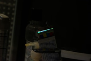 A dark setting with several bottles and a box that has a reflective strip showing a spectrum of colors. The lighting is low, creating a dim environment.