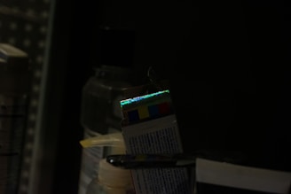 A dark setting with several bottles and a box that has a reflective strip showing a spectrum of colors. The lighting is low, creating a dim environment.