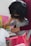 A young child engages in a creative activity, painting with their fingers on paper, while an adult assists and guides them. The child, adorned in a pink tutu-like skirt, appears focused on the task. The setting includes a pink chair and a bright yellow frame in the background.