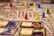 A close-up of a detailed board game in progress with various colored game pieces, such as red, yellow, blue, and green, placed on a textured map. There are also several cards with text and images on them, adding to the intricate and immersive nature of the game.