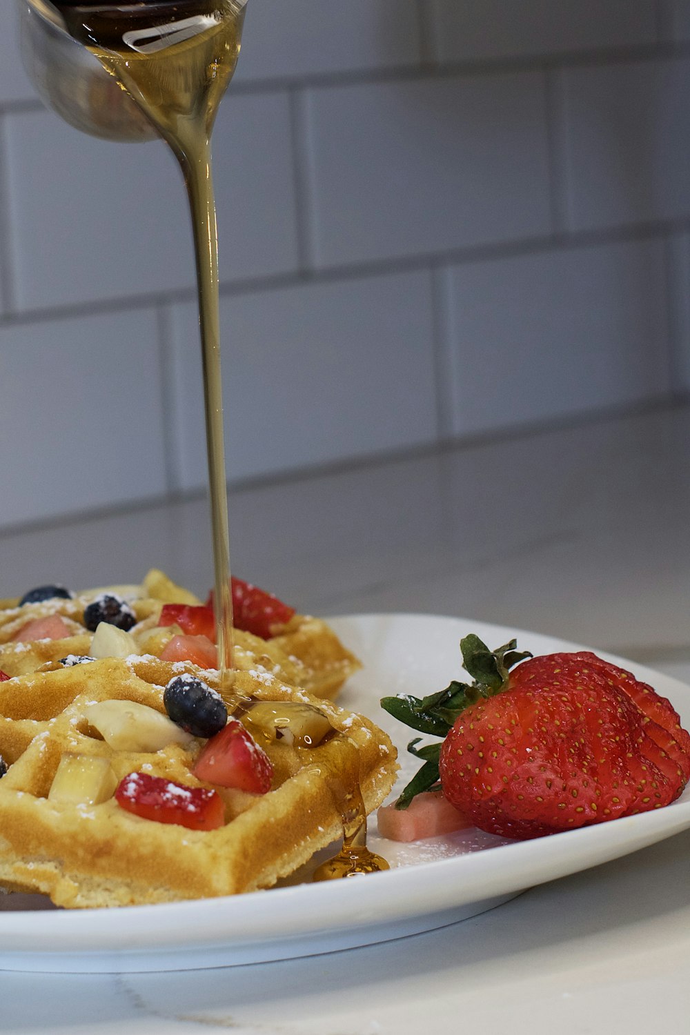 a waffle being drizzled with syrup with strawberries and blueberries