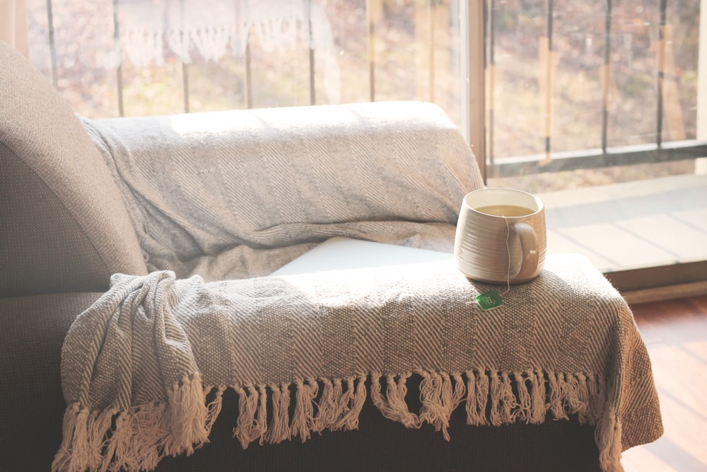 a coffee cup sitting on a couch next to a window