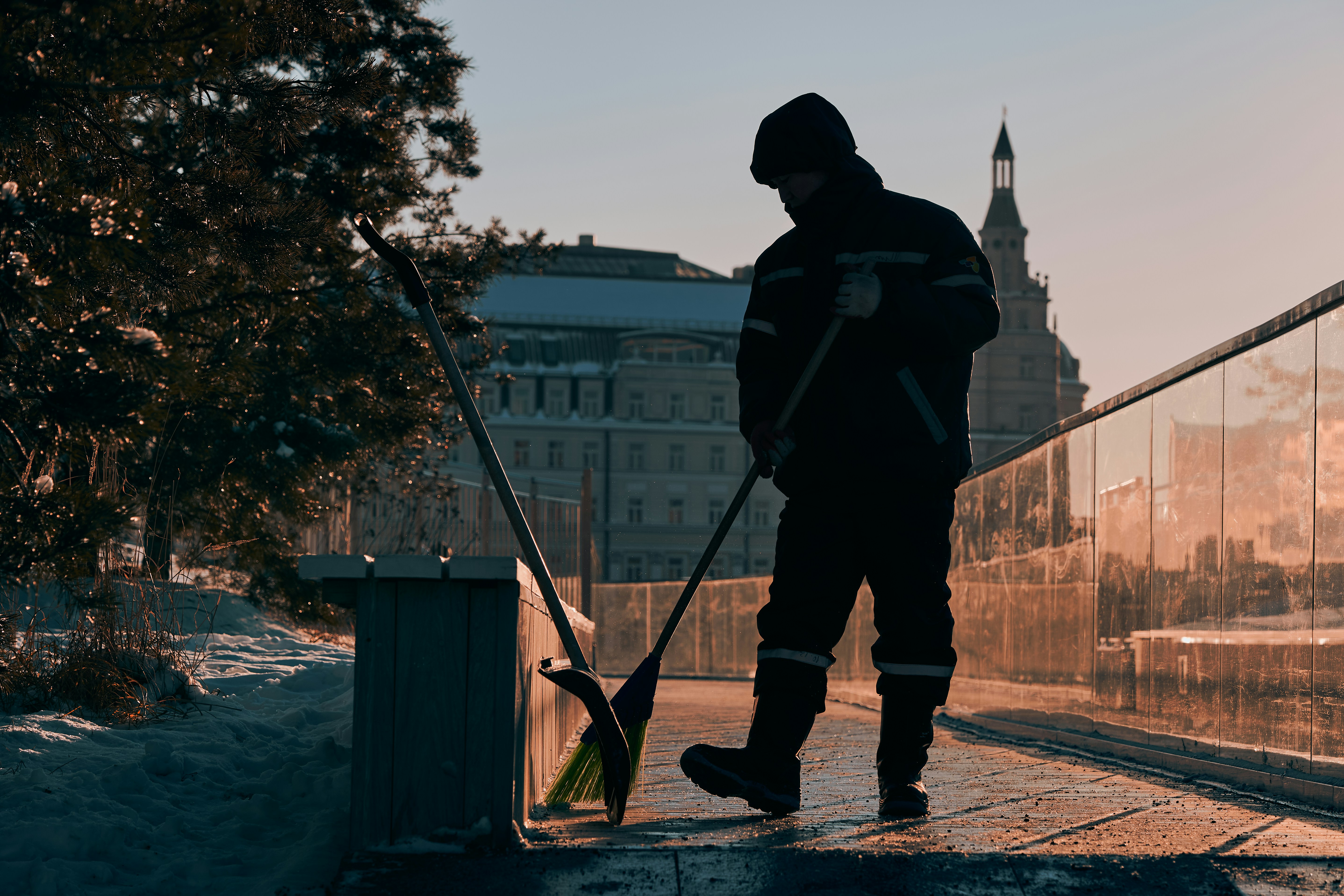 A maintenance worker clears snow from a path with a broom.