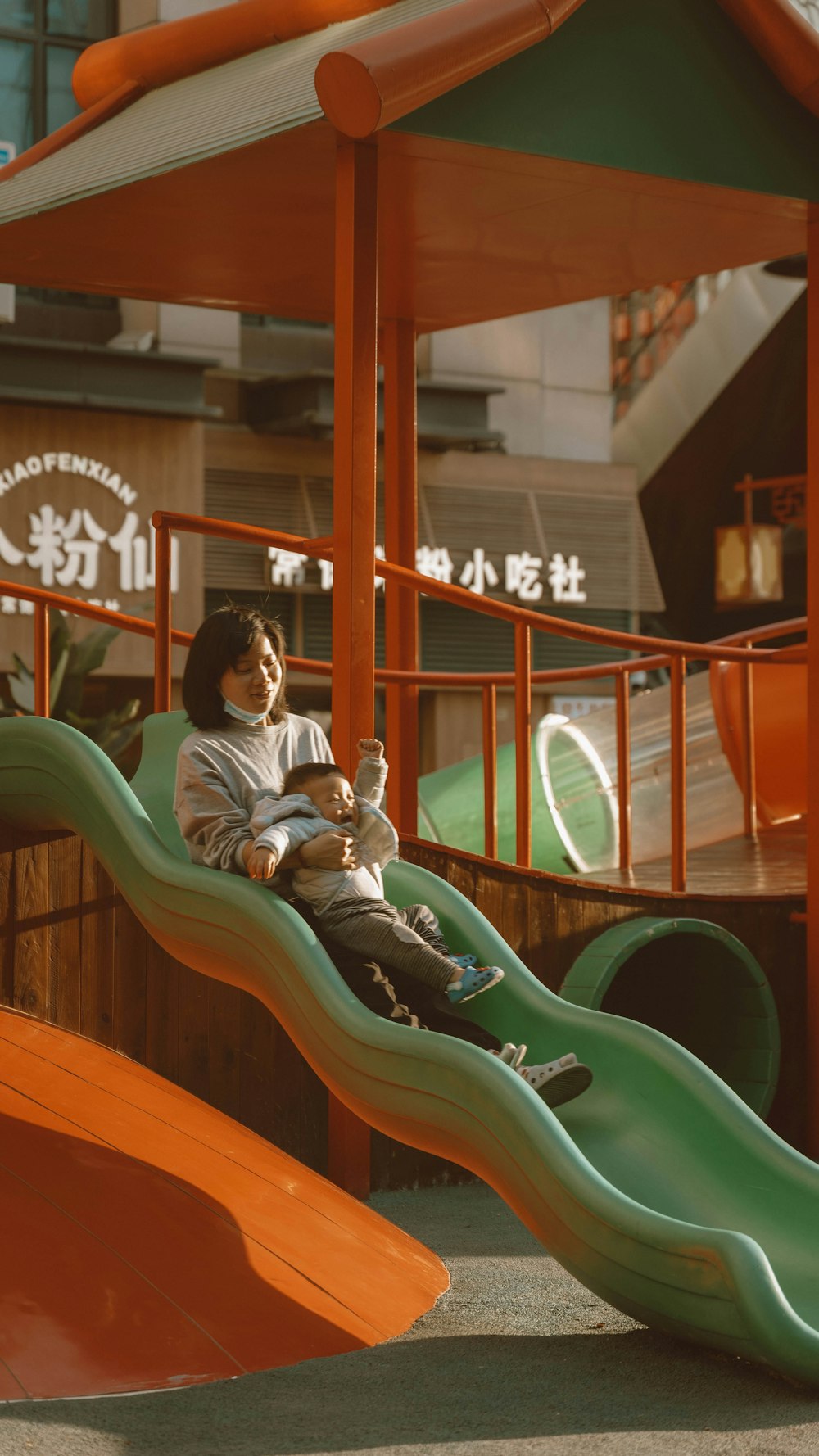 a young boy sitting on a slide in a playground
