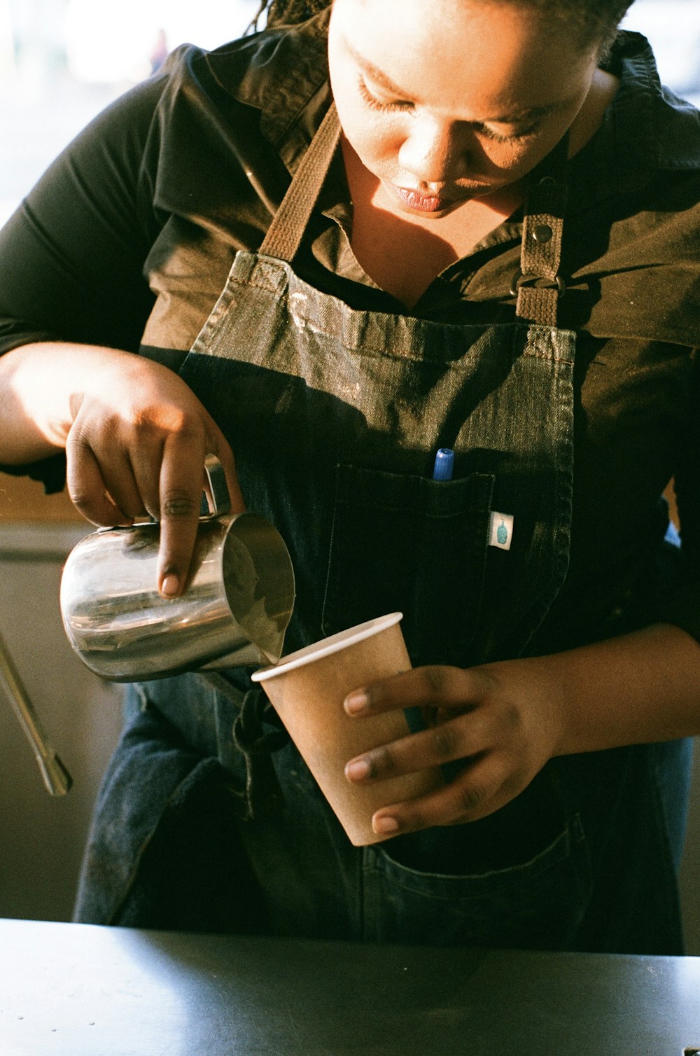 a woman pouring a cup of coffee into a paper cup