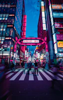 A bustling city street scene with people crossing and bright signs.