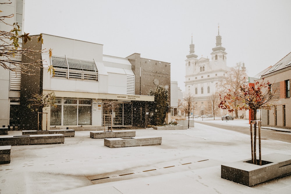 a snowy street with benches and a building in the background