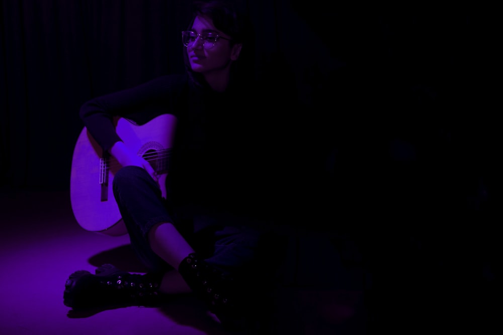 a woman sitting in the dark with a guitar