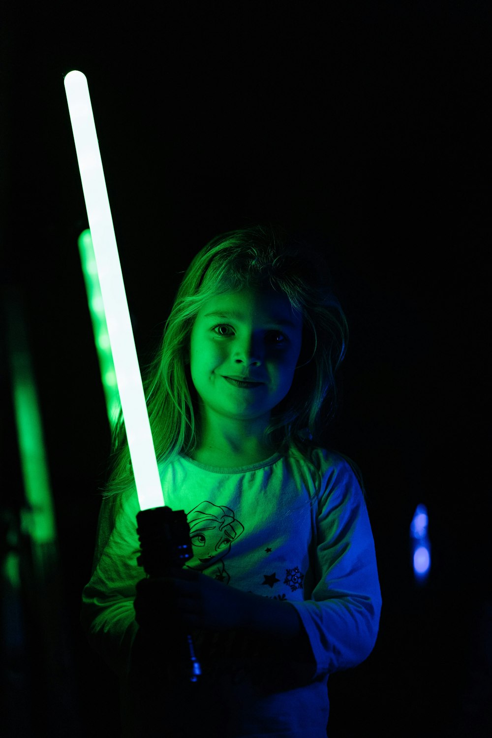 a little girl holding a light saber in a dark room