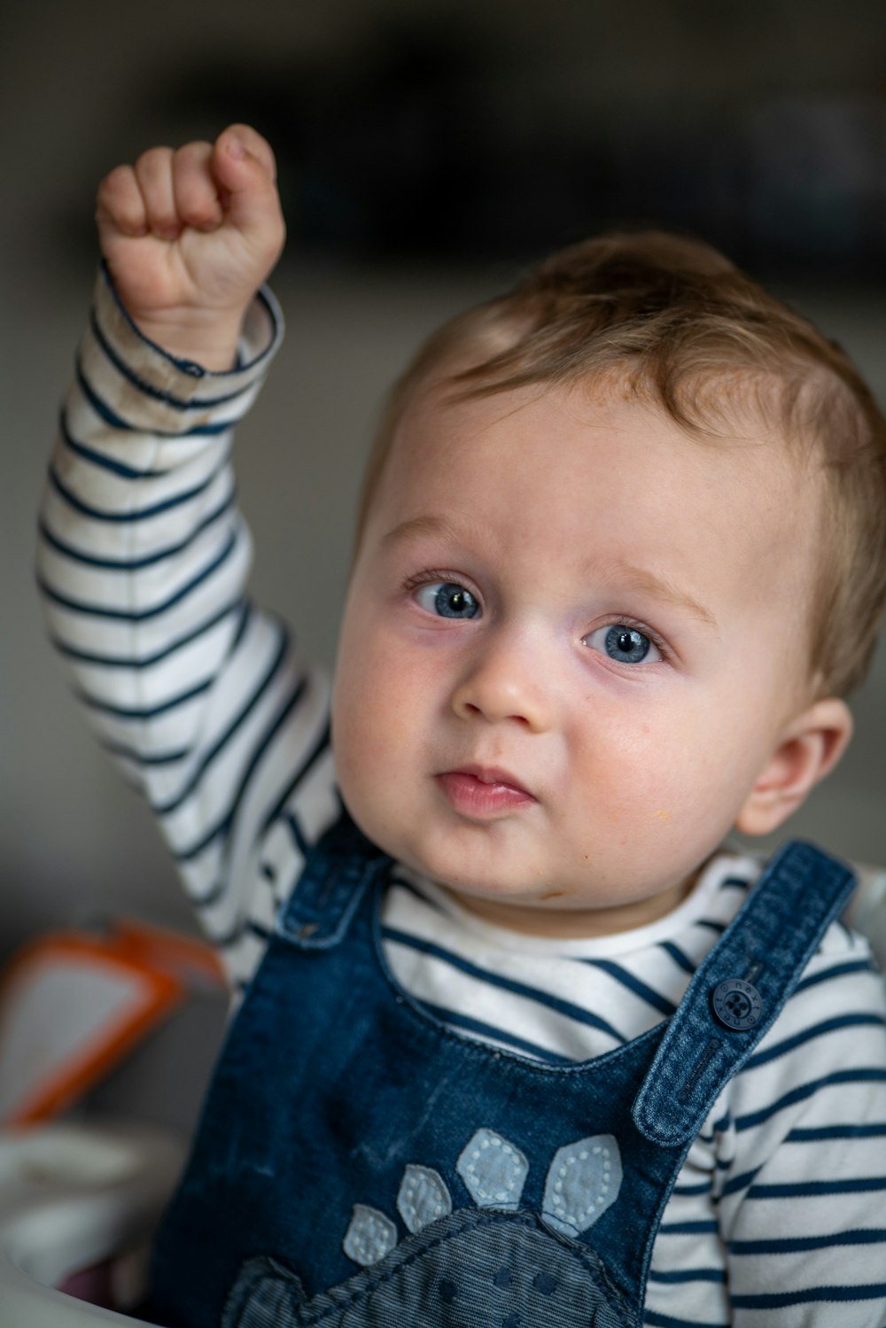 a baby in overalls holds his hand up in the air