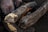 A close-up of two pieces of wood being arranged to start a campfire. One can see hands holding a lighter, with small flames and smoke starting to emerge between the logs.