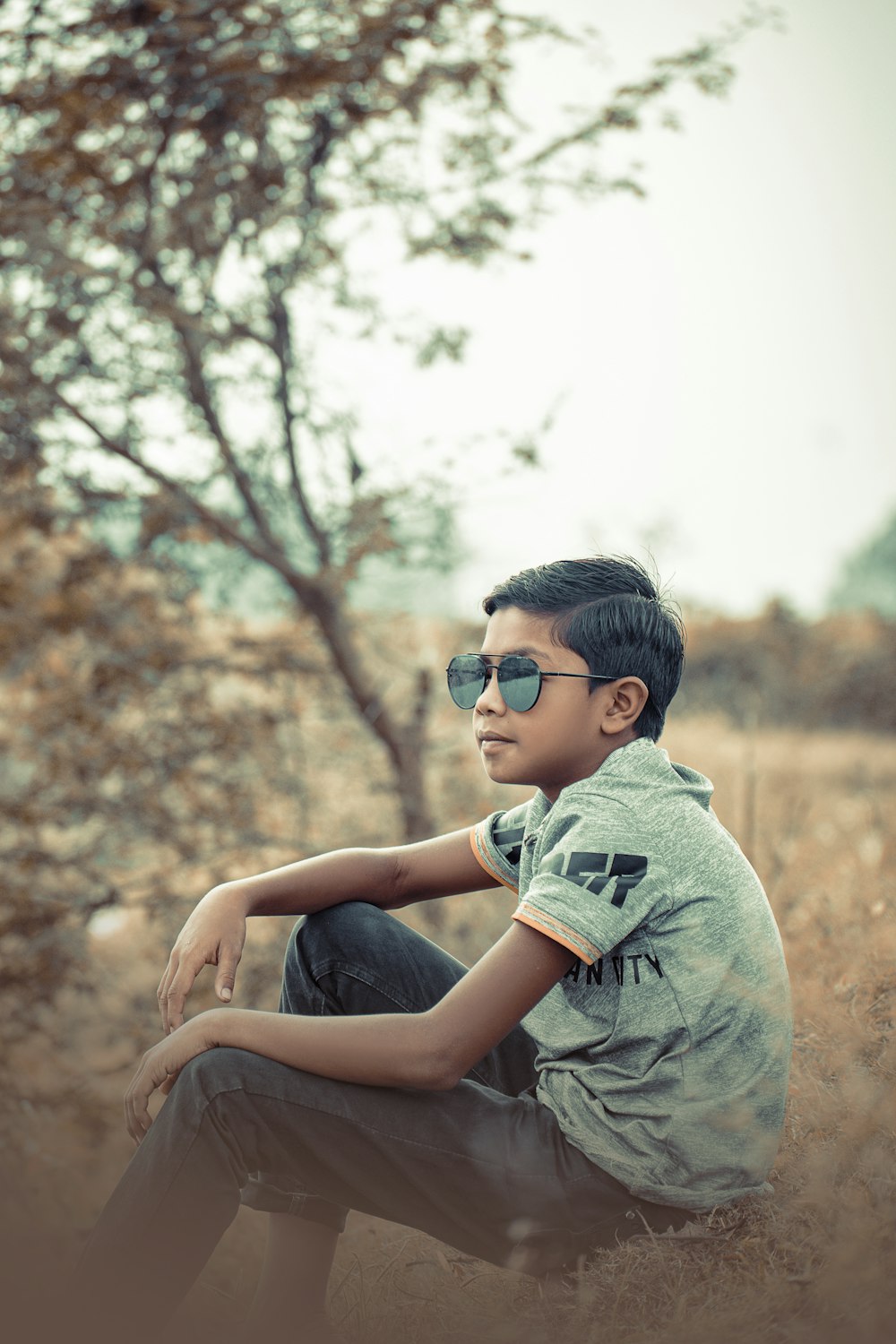a young boy sitting in a field with a tree in the background