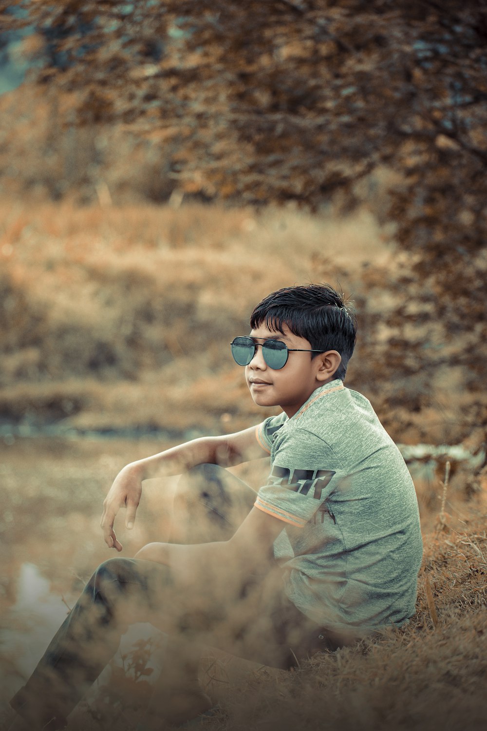 a young man sitting in a field wearing sunglasses