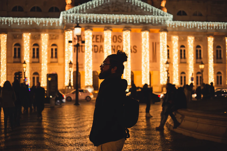 The Teatro Nacional D. Maria II on Rossio lit with Christmas lights at night, with people in the square