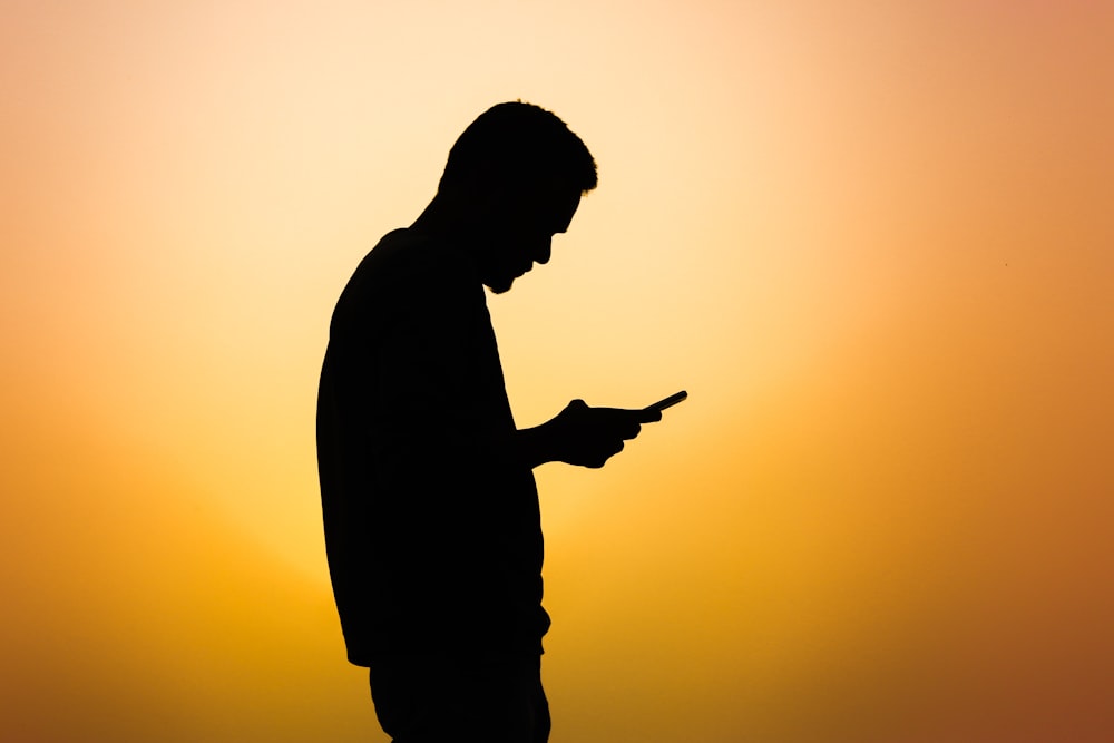 a silhouette of a man using a cell phone