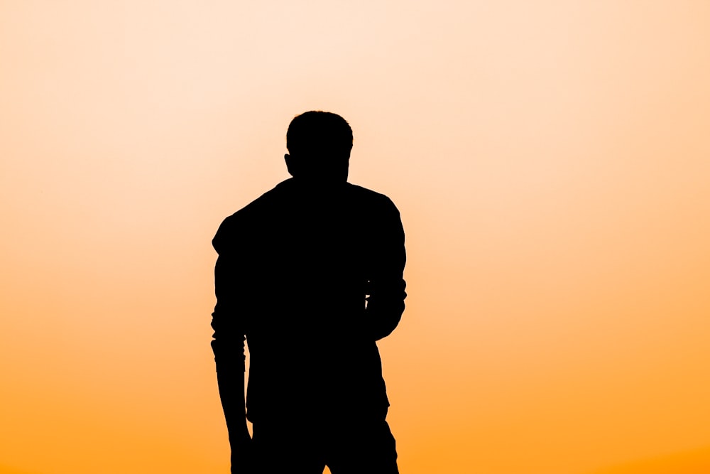 a silhouette of a man standing in front of an orange sky
