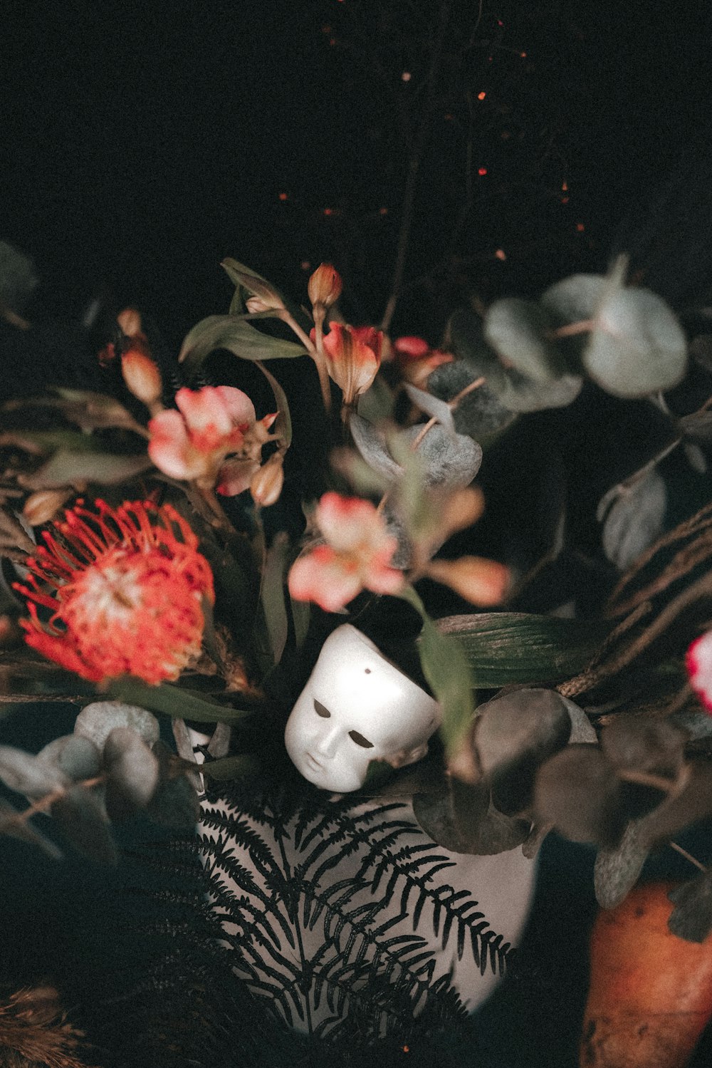 una máscara blanca rodeada de flores y hojas