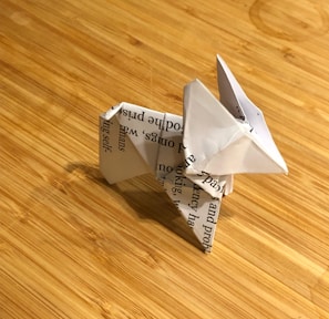 An origami figure made from a piece of paper with printed text, resembling an animal, is placed on a wooden surface with visible grain patterns.