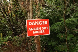 a red danger sign sitting on the side of a forest