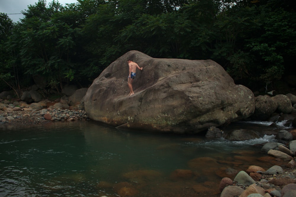 a man standing on top of a large rock next to a river