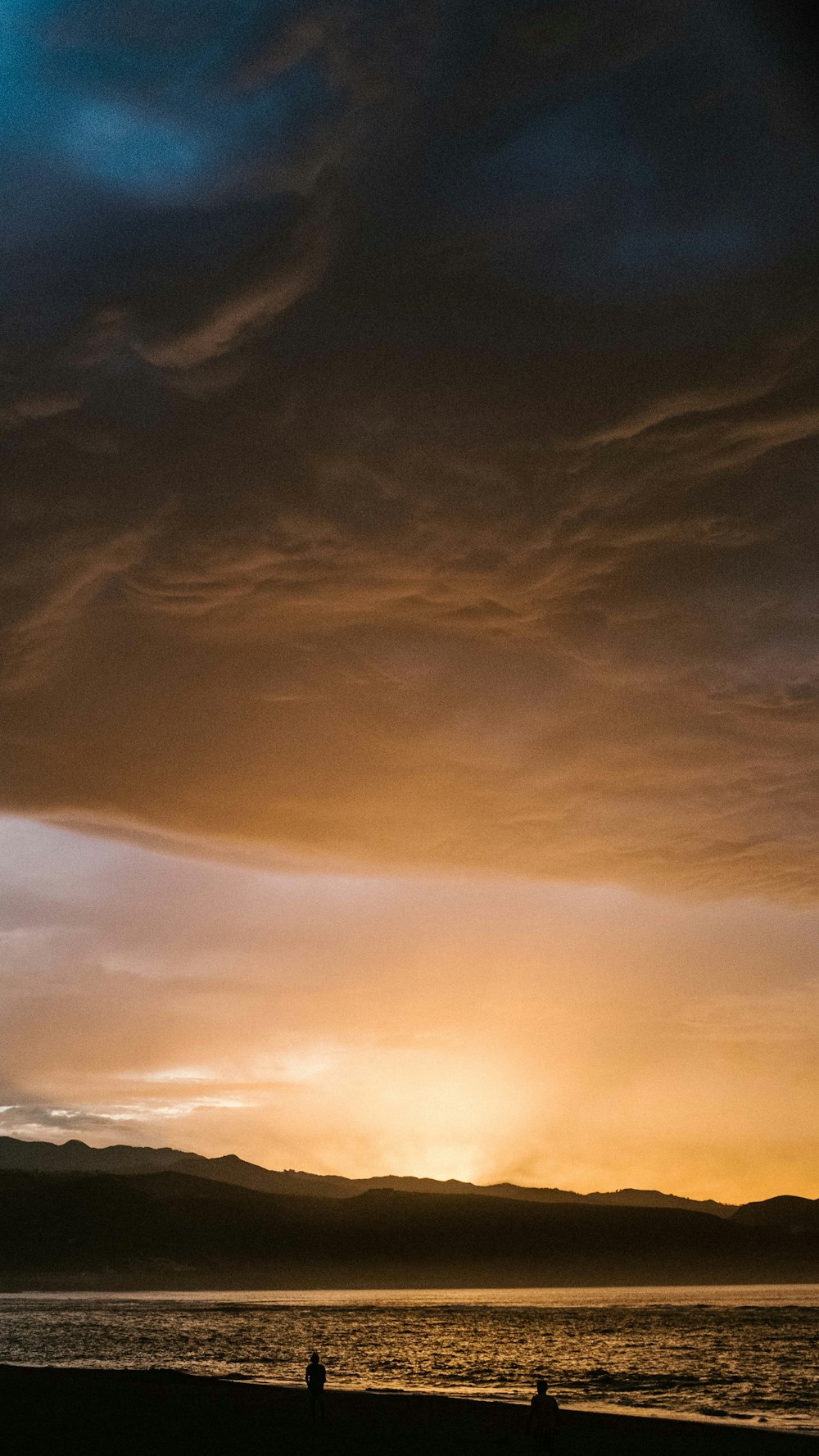 a couple of people standing on top of a beach under a cloudy sky