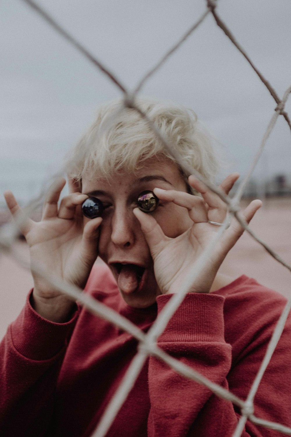 a woman holding her hands up to her face behind a chain link fence