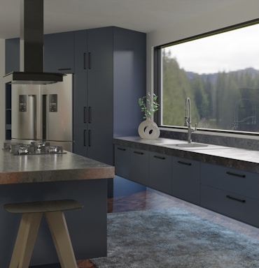 A modern kitchen interior features sleek and dark cabinetry with a glossy refrigerator. The countertop holds a contemporary ceramic vase with a green plant near a large window offering a view of trees. An island with a black stove and ventilation hood enhances the sophisticated look, and a textured rug covers part of the wooden floor.
