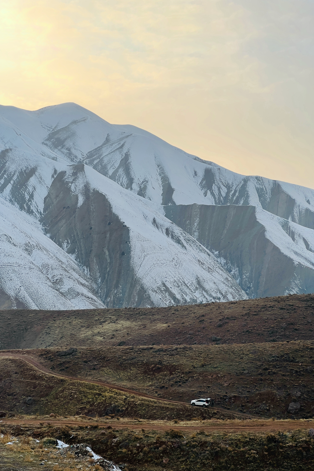 a snowy mountain range with a dirt road in the foreground