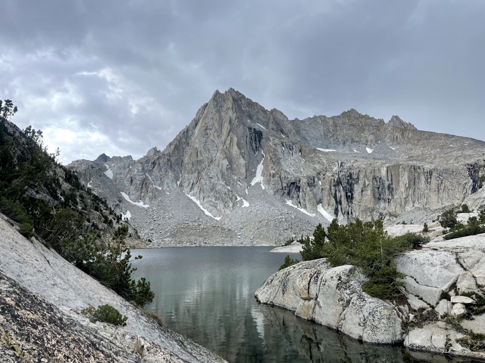 a lake surrounded by rocks and mountains under a cloudy sky