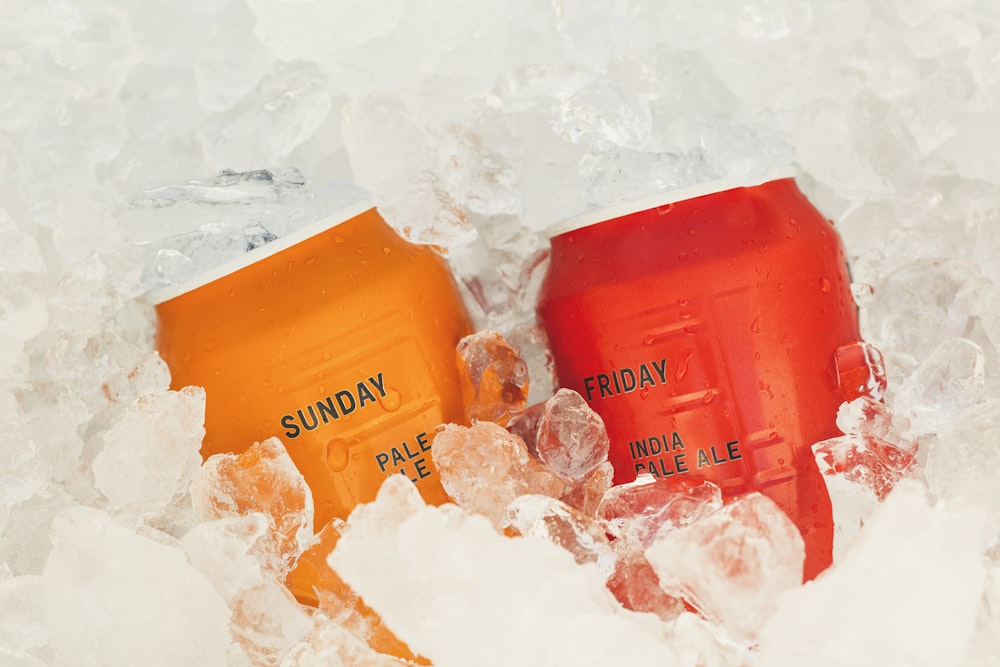 two orange and red soda cans sitting in ice