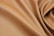 A close-up view of smooth, tan-colored leather fabric with gentle folds and a soft texture. The leather has a subtle sheen and fine grain, giving it an elegant appearance.