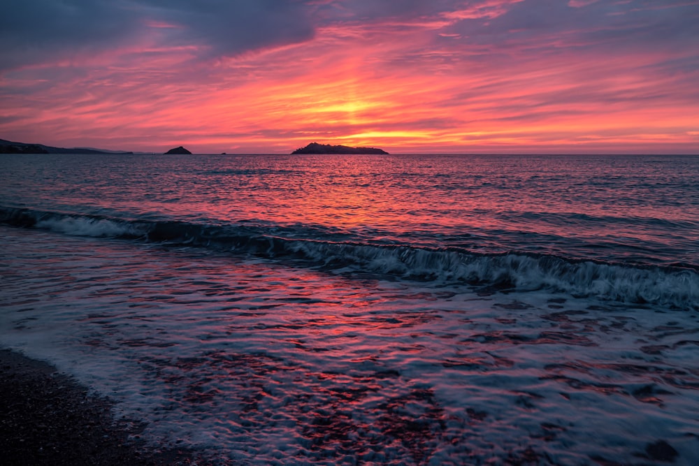 a sunset over the ocean with a small island in the distance