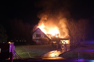 a house on fire at night with a house on fire in the background