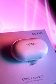 A white earbud charging case labeled 'OPPO' rests on top of a box with the product name 'OPPO Enco W11 True Wireless Headphones'. The background features a vibrant pink and purple gradient, creating a modern and stylish look.