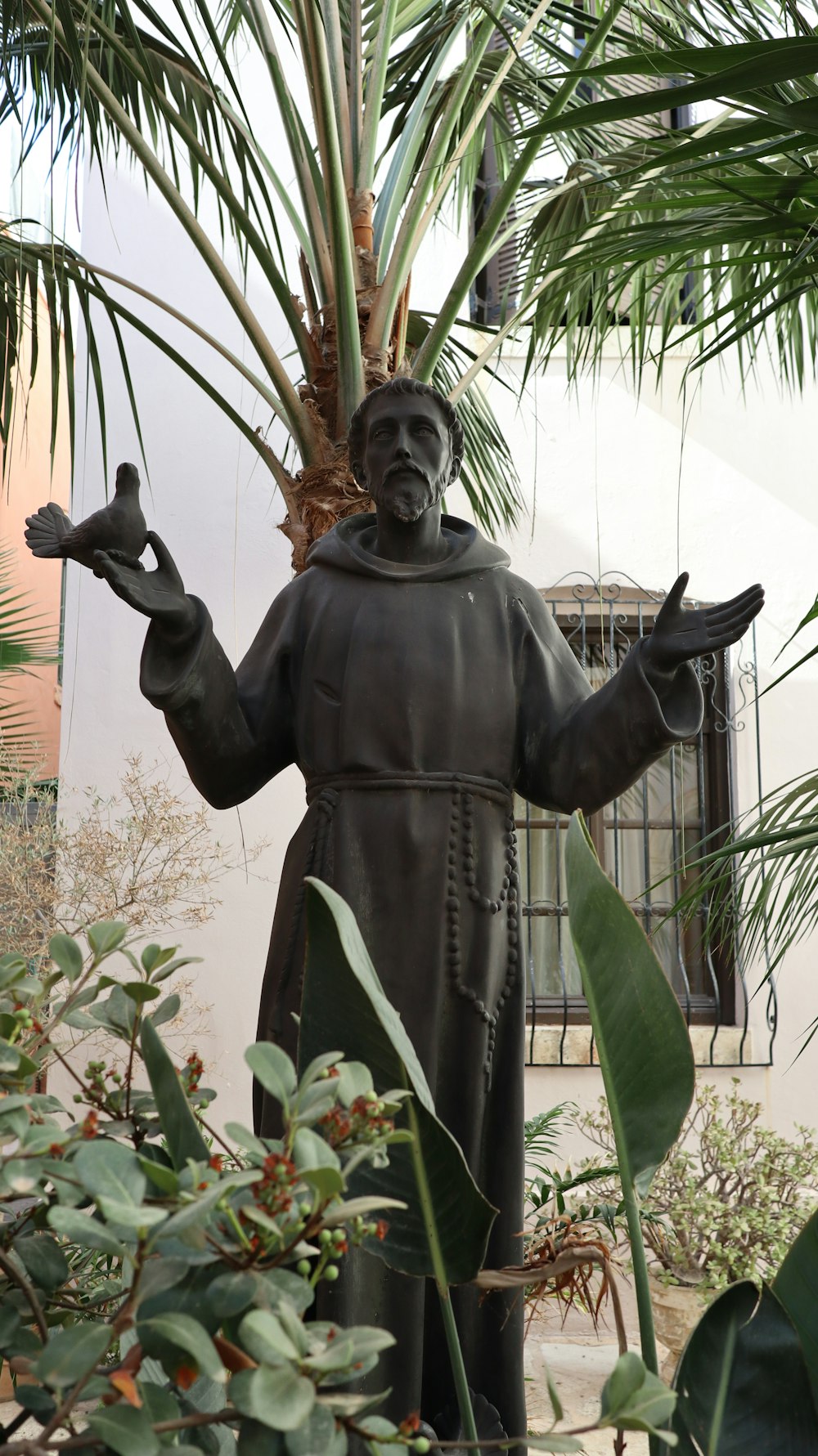 a statue of a man holding two hands in front of a palm tree