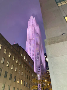 Elegant commercial skyscraper framed by a clear blue sky with soft purple lighting highlights.