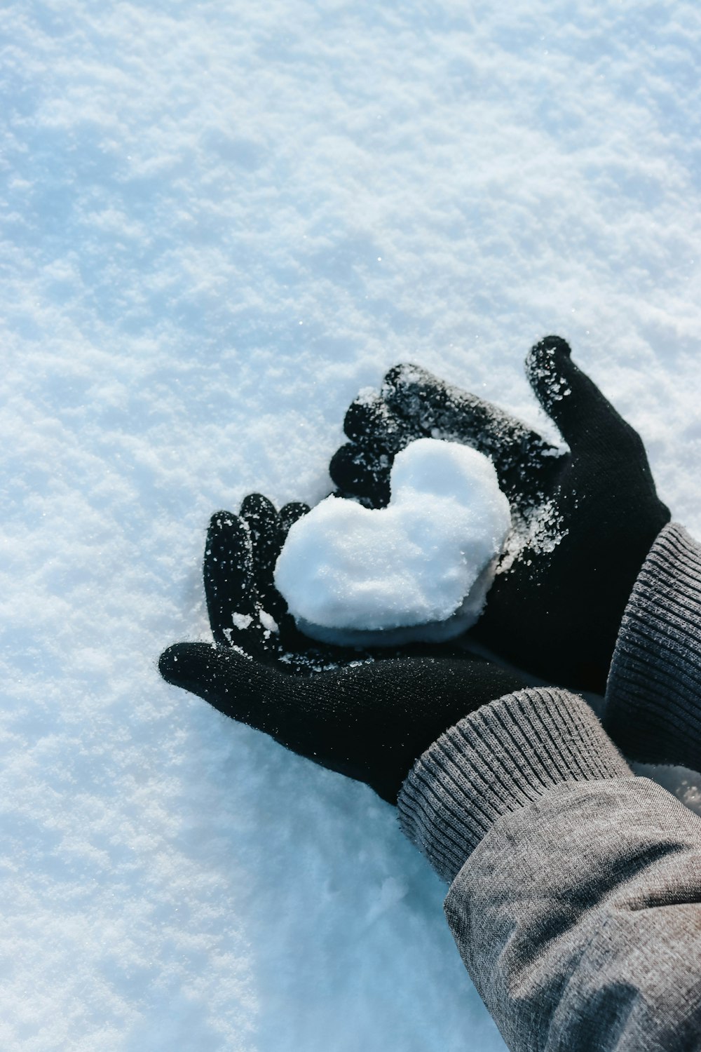 a person's hand holding a snow heart in the snow